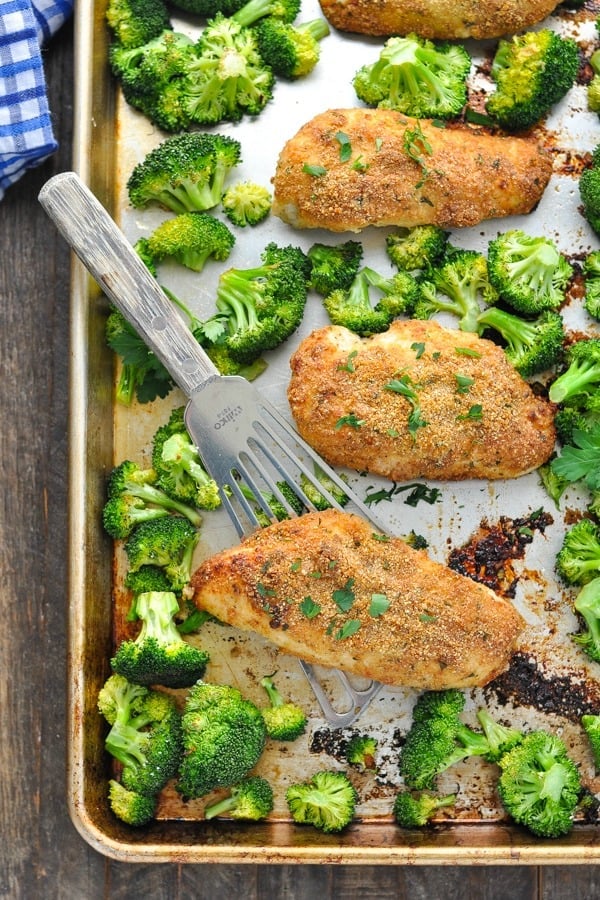 Overhead shot of garlic parmesan chicken and broccoli on a sheet pan with a spatula