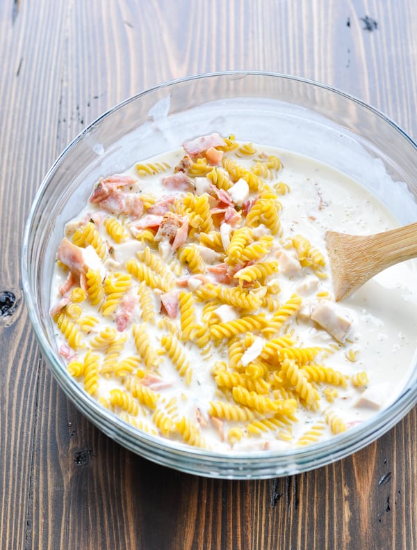 Raw ingredients for chicken bacon ranch pasta in a glass mixing bowl with wooden spoon