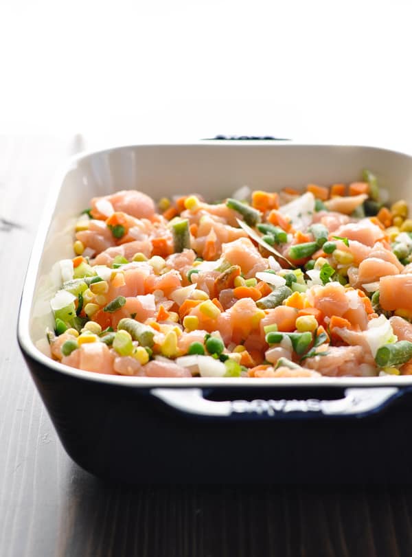 Frozen mixed vegetables with raw diced chicken in blue baking dish