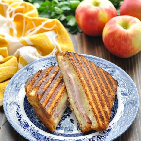 Ham and Cheese Panini Sandwich on a blue and white plate with fresh apples in the background