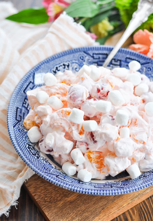 Pink Ambrosia Salad in a blue and white bowl with a pink and white stripe cloth napkin in the background