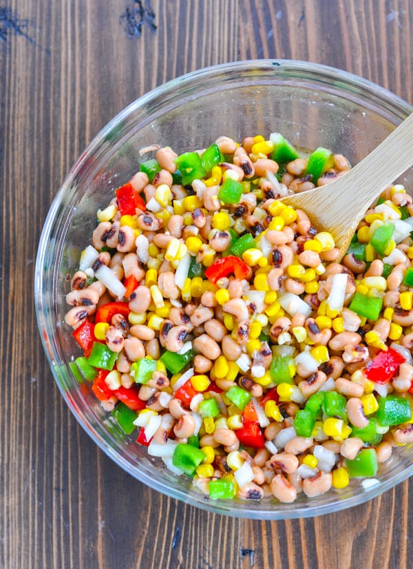 Overhead shot of texas caviar stirred together with a wooden spoon in a glass mixing bowl