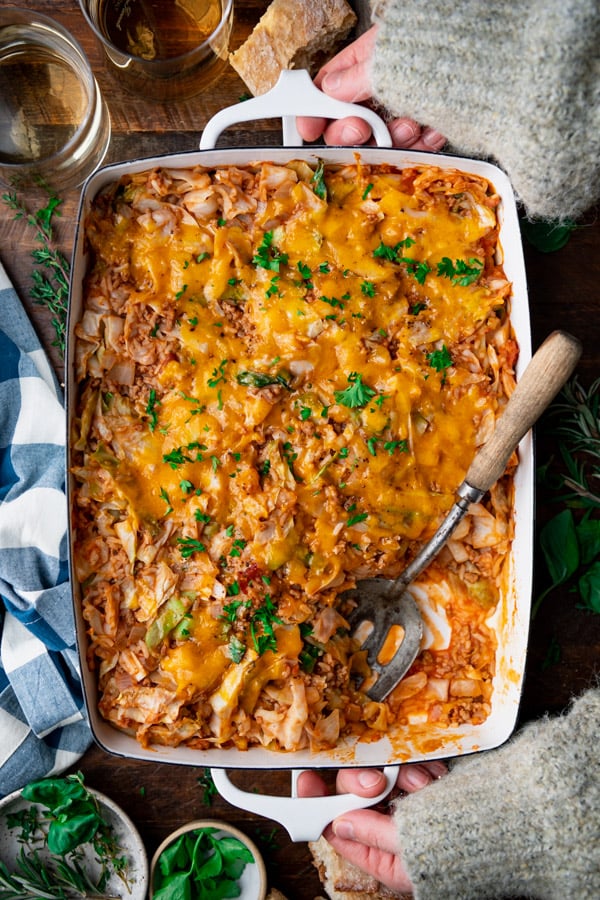 Hands holding a white baking dish full of the best cabbage roll casserole recipe