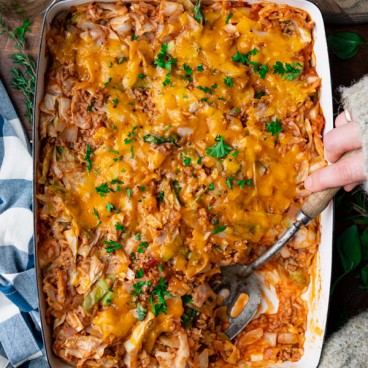 Hands serving cabbage roll casserole from a dish