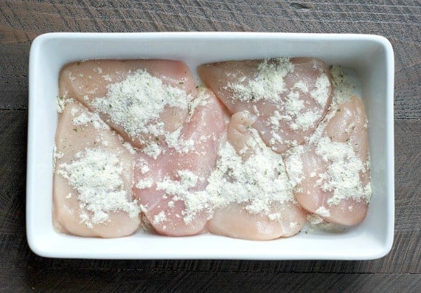 Rae chicken breasts arranged in a white casserole dish, sprinkled with ranch seasoning mix.