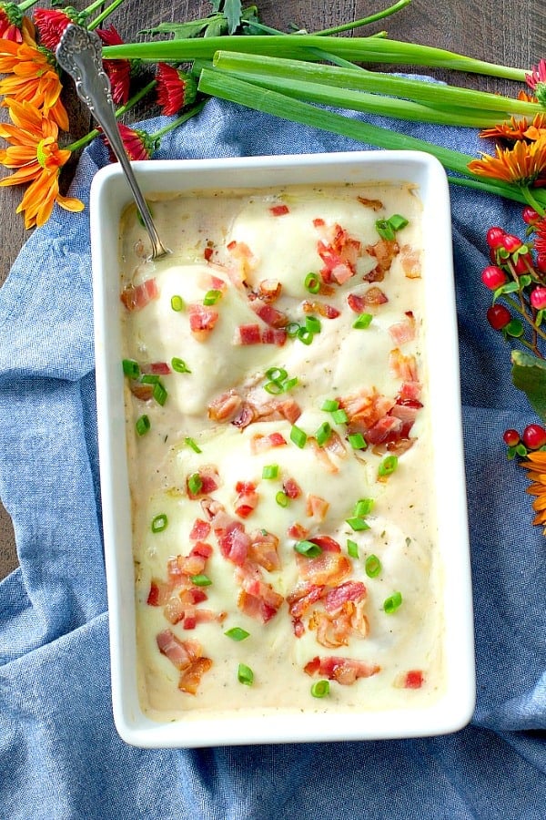 Overhead shot of baked chicken breast in white dish with bacon and cheese