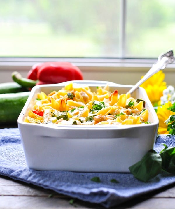 A side shot of summer pasta with zucchini in a casserole dish with a serving spoon
