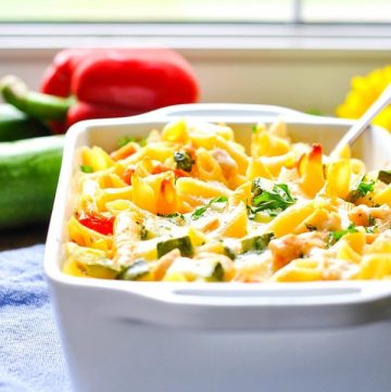 Summer pasta with zucchini, tomatoes and corn in a white casserole dish in front of a window