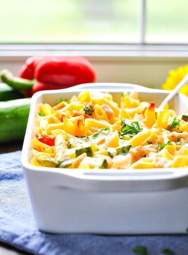Summer pasta with zucchini, tomatoes and corn in a white casserole dish in front of a window