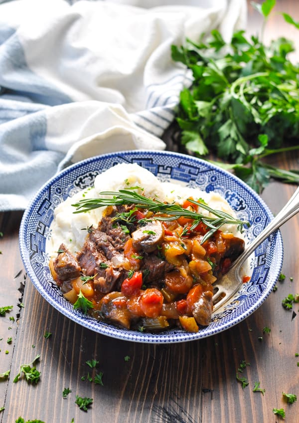 Swiss steak in a bowl surrounded by fresh herbs