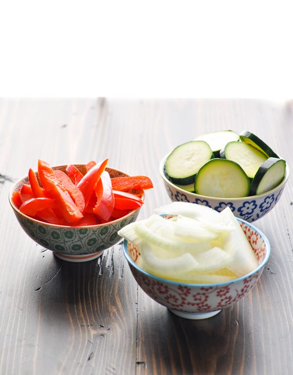 Three bowls of chopped fresh bell peppers, zucchini and onion