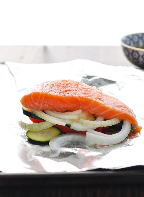Piece of raw salmon on top of fresh vegetables on a piece of aluminum foil