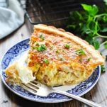 Quiche Lorraine on a plate with a bite on a fork and fresh parsley garnish