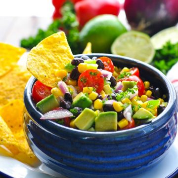 Blue bowl full of Black Bean and Corn Salad with tortilla chip for dipping