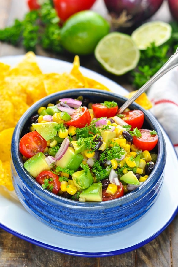 Silver serving spoon in a bowl of Black Bean and Corn Salsa surrounded by chips
