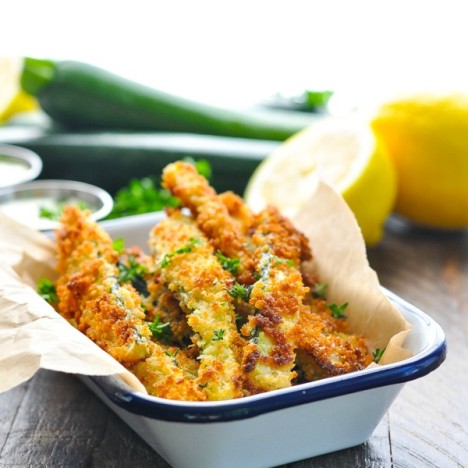 Bright shot of crispy zucchini fries in a blue and white dish with lemons in the background