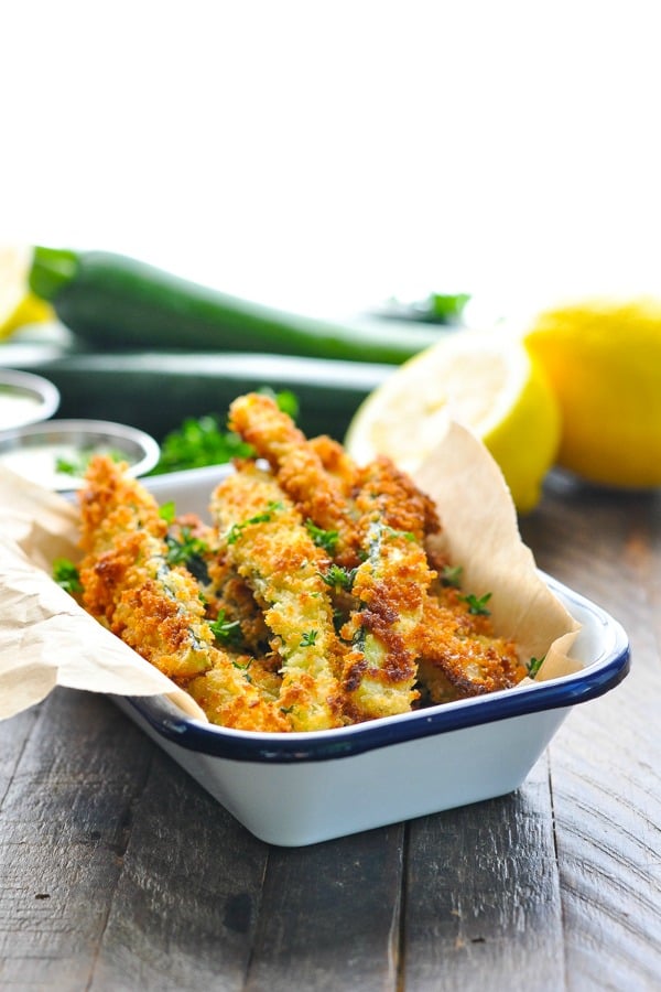 Bright shot of crispy zucchini fries in a blue and white dish with lemons in the background