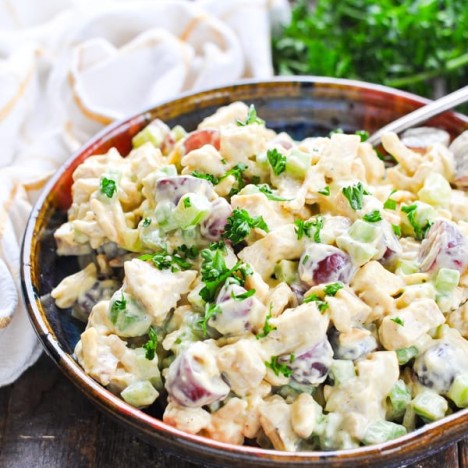 Curried chicken salad with grapes and garnished with parsley in a serving bowl