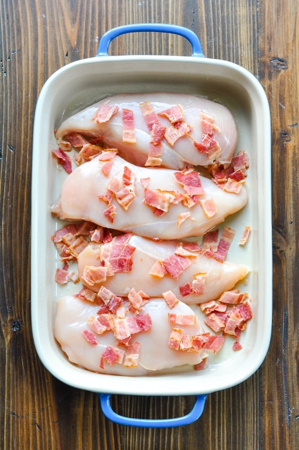 Raw chicken breasts and chopped cooked bacon in a blue casserole dish