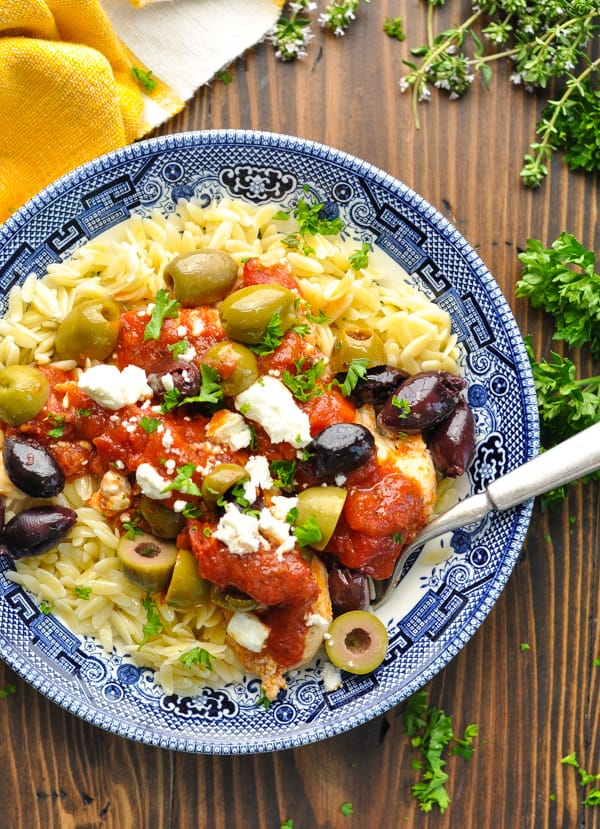 Close overhead shot of bowl of baked chicken tenderloins with olives and feta over orzo pasta