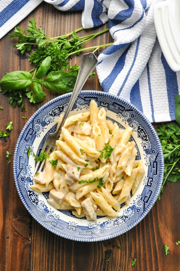 Overhead shot of parmesan pasta with chicken in a blue and white bowl with fresh herbs on top