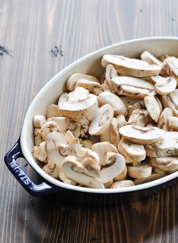 Raw sliced mushrooms over chicken in a blue baking dish