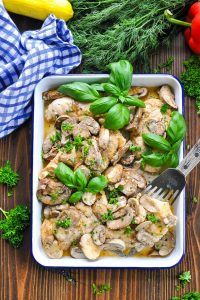 Long overhead shot of baked chicken and mushrooms garnished with fresh herbs