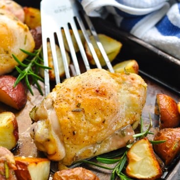 Rosemary chicken on a serving spatula surrounded by potatoes