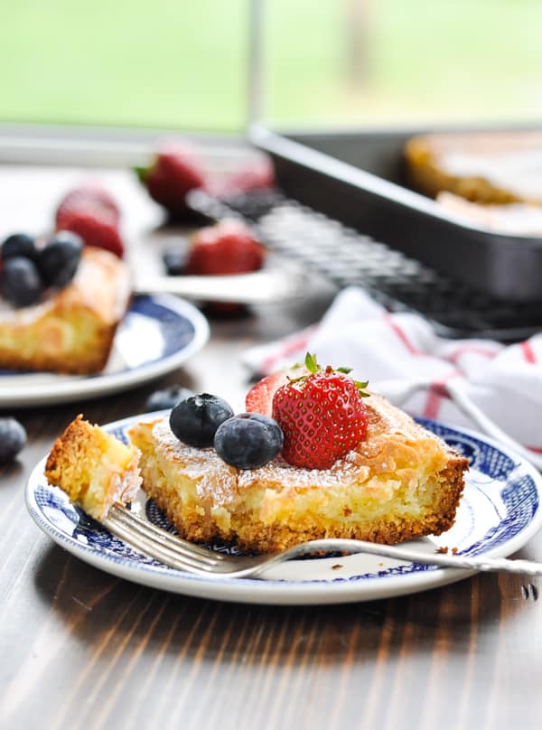Slice of gooey butter cake with fresh berries on a plate with a bite on a fork