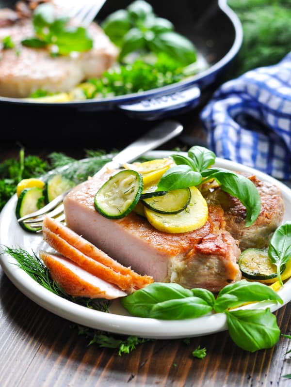 Close up shot of skillet pork chops on a plate with fresh vegetables and herbs