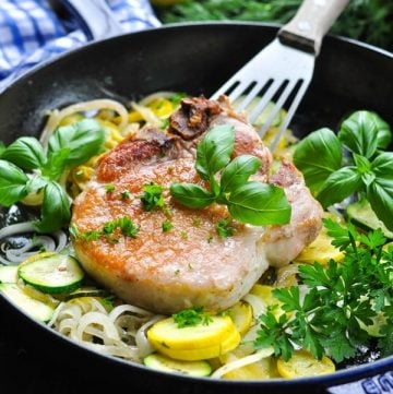 Pan fried pork chops in a skillet with zucchini and squash