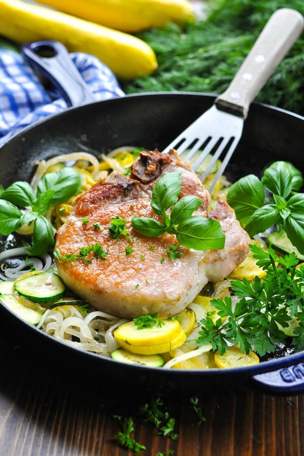 Pan fried pork chops in a skillet with zucchini and squash