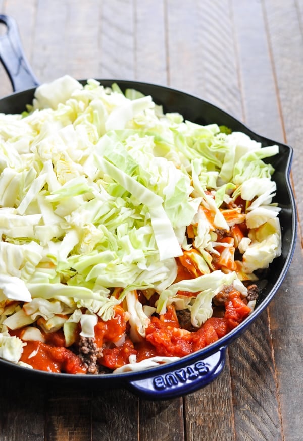 Raw cabbage and tomatoes in a skillet with ground beef