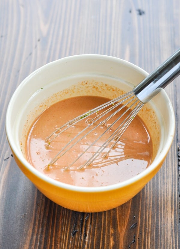 A creamy coconut peanut butter curry sauce mixed together in a ceramic bowl with a metal whisk.