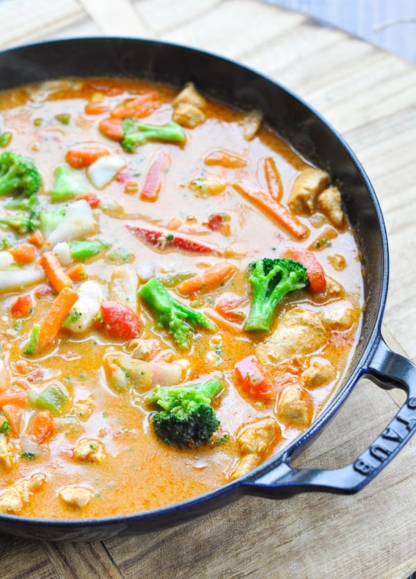 A closeup image of a skillet of homemade curry chicken cooked in a curry sauce with broccoli, carrots, and vegetables.