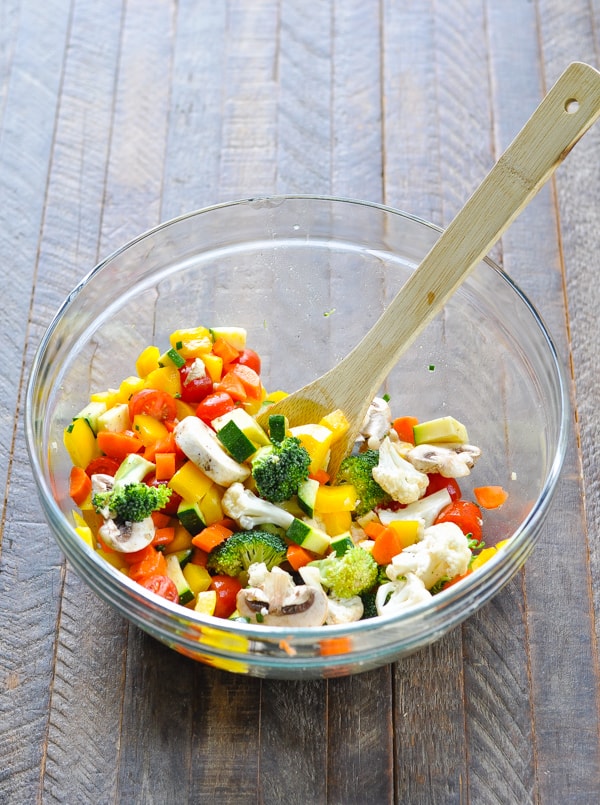 Marinated vegetable salad in a glass mixing bowl with wooden spoon