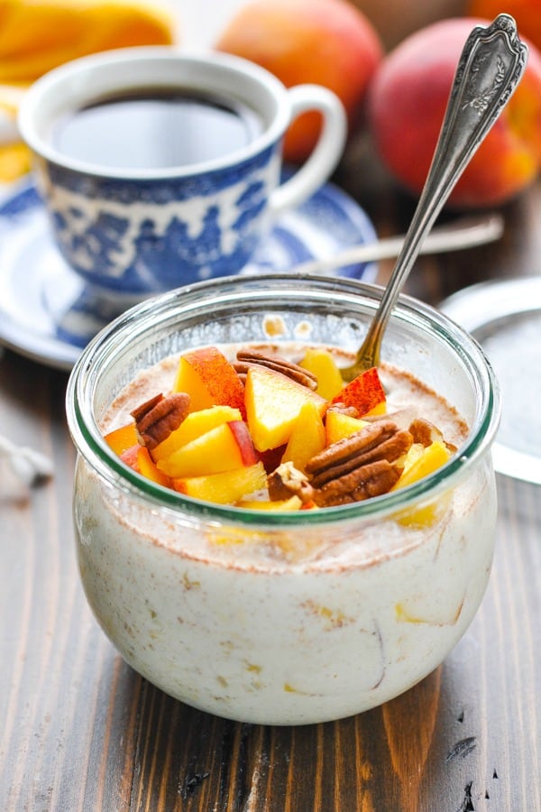 Glass bowl full of overnight refrigerator oatmeal with peaches and pecans