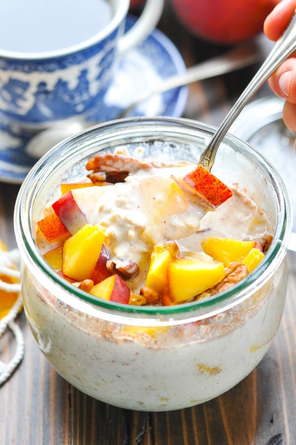 Close up shot of refrigerated oatmeal with fresh peaches and pecans in a glass bowl with a spoon
