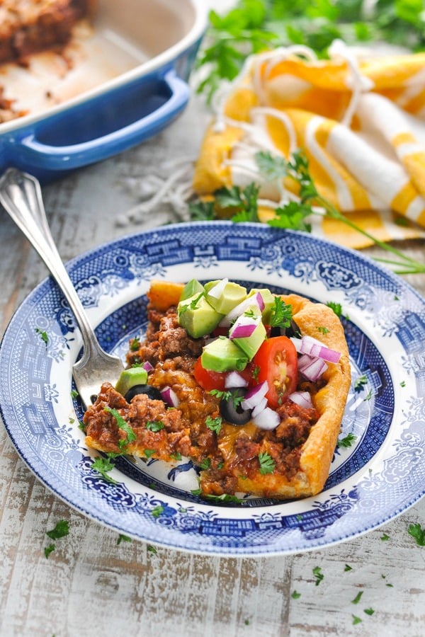 Close up front shot of a piece of taco casserole with crescent dough on a plate with toppings