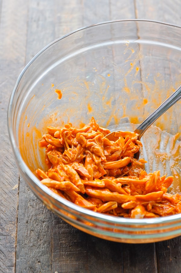 Shredded chicken tossed with buffalo wing sauce in a glass mixing bowl