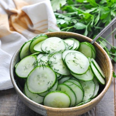 Close up shot of marinated cucumbers in a serving bowl garnished with fresh dill