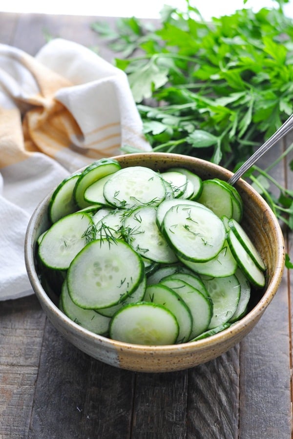 Close up shot of marinated cucumbers in a serving bowl garnished with fresh dill