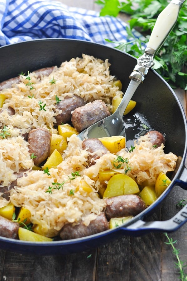 Close up shot of cooked beer brats with potatoes and sauerkraut in a skillet