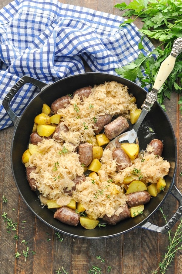 Long overhead shot of an easy bratwurst recipe with sausage and potatoes in a cast iron skillet