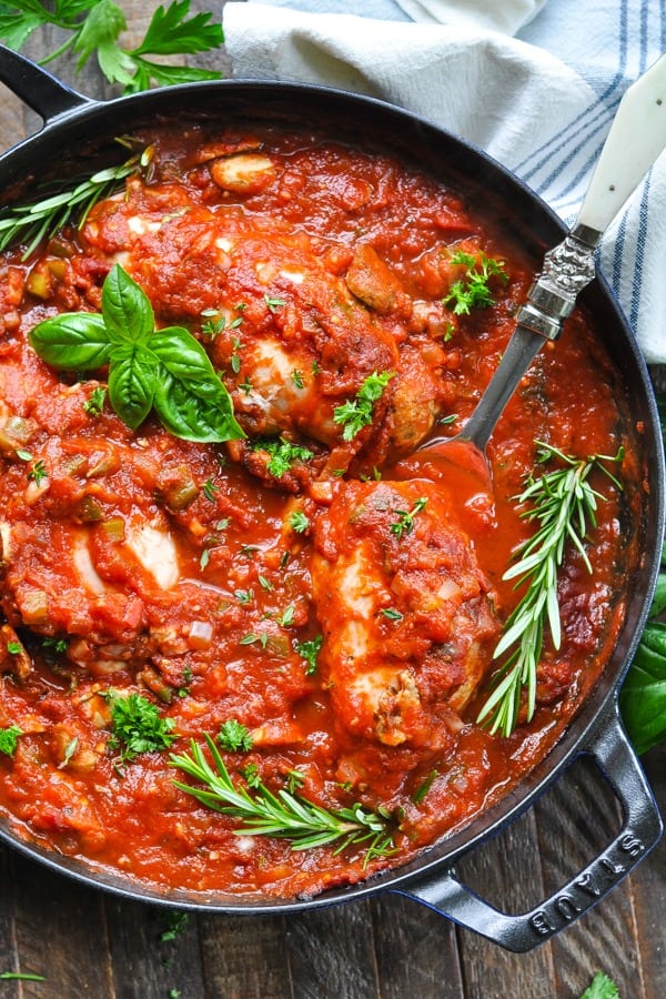 Long overhead shot of baked boneless skinless chicken cacciatore recipe in a skillet with fresh herbs