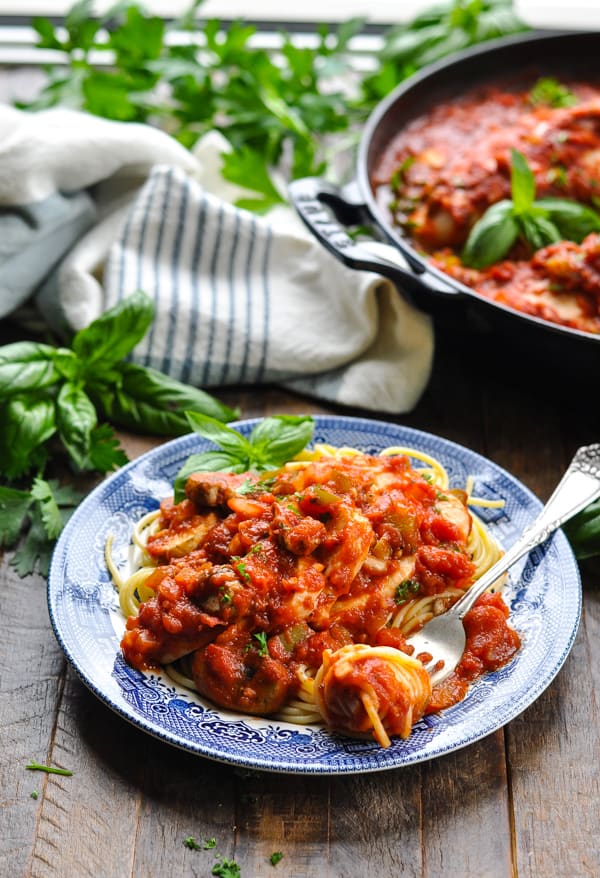 Chicken Cacciatore recipe on a blue and white dinner plate with a fork and pasta