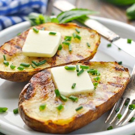Close up front shot of grilled potatoes on a plate with butter and chives