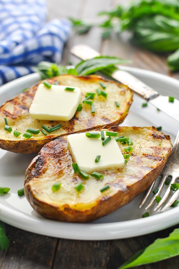 Close up front shot of grilled potatoes on a plate with butter and chives