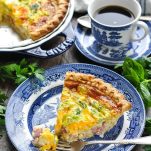 Photo of slice of ham cheddar and broccoli quiche on a plate with a bite on a fork