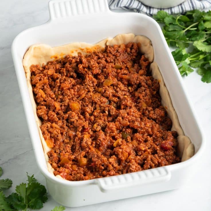 Process shot showing how to assemble a taco casserole with crescent rolls and ground beef.